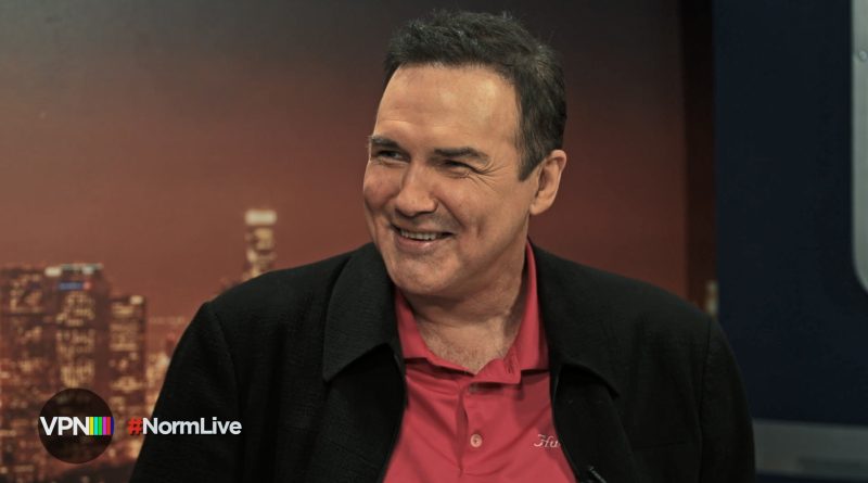 "Man smiling in a studio setting with a city skyline background, wearing a red polo shirt and dark jacket; VPN and #NormLive logos visible in corner, warm lighting."