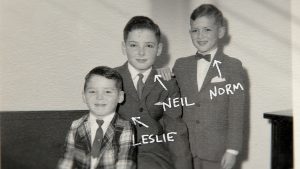 "Three children dressed in suits posing for a black-and-white portrait indoors, with handwritten labels "Leslie," "Neil," and "Norm" and arrows pointing to each of them."